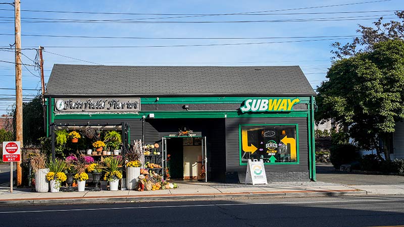photo of a house with a gray roof in which there is a flower shop and a subway sandwich store
