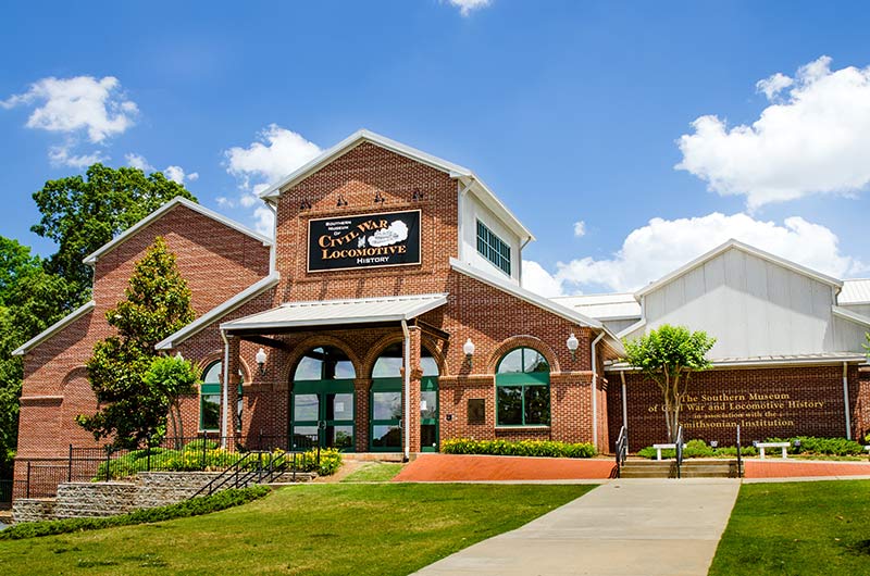 a red brick building resembling a gouse with green fields in front